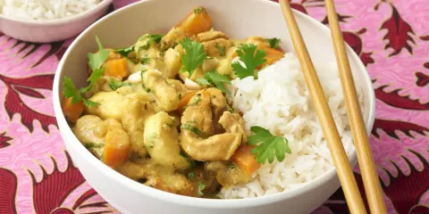 Ein köstliches Bananencurry mit Hähnchen, Karotten und Reis, garniert mit Koriander. Chopsticks liegen bereit.