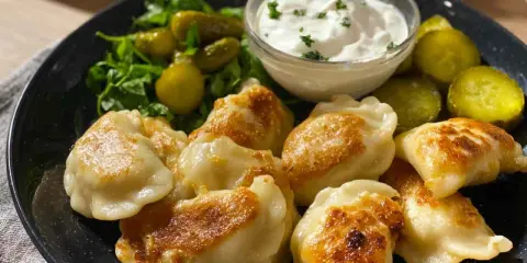 Złociste ruskie pierogi podane z kwaśną śmietaną, ogórkami kiszonymi i zieloną sałatką. Pyszny, tradycyjny posiłek.