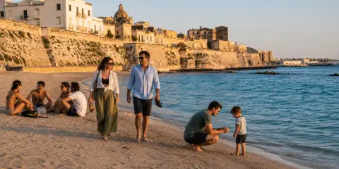 Famiglia passeggia sulla spiaggia di **Salento, Italia**, con un borgo storico sullo sfondo.
