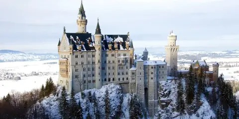 Zamek Neuschwanstein w zimowej scenerii, otoczony ośnieżonymi drzewami i krajobrazem.