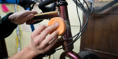 Hände polieren den Fahrradrahmen mit einem orangen Schwamm, um den Fahrradlack auszubessern.