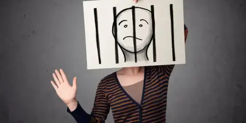 Osoba trzyma tabliczkę z rysunkiem twarzy za kratami. Czy to paranoik, który czuje się uwięziony?