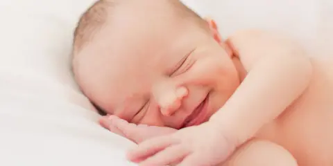 Un bebé duerme plácidamente, con una sonrisa que nos hace preguntar porque sonrien los bebes. Su carita refleja paz y felicidad.