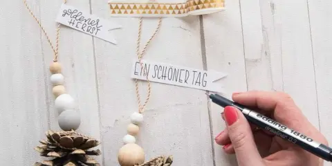Déco Noël pomme de pin à faire soi-même : des suspensions naturelles avec perles en bois et messages personnalisés.