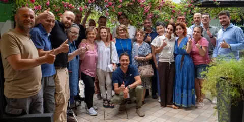 Un gruppo di persone sorridenti festeggia la primavera viserba sotto un pergolato fiorito.