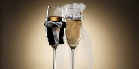 Dwa kieliszki szampana, jeden w stroju pana młodego, drugi z welonem panny młodej. Idealne wino dla pary młodej na toast.