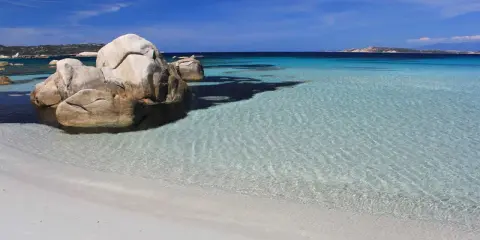 Spiaggia bianca e rocce granitiche sull'isola della Maddalena, con acque cristalline e un cielo azzurro intenso.