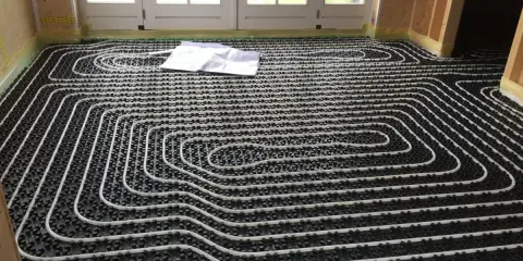 Instalación suelo radiante con tuberías blancas sobre paneles negros. Un plano yace sobre el suelo.