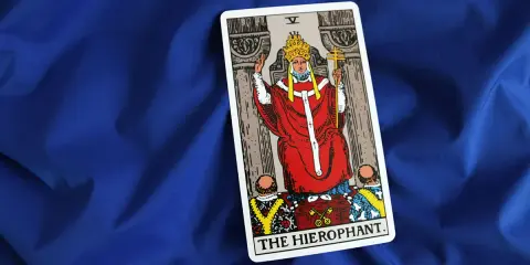 Karta Tarota "The Hierophant" na niebieskim tle. Postać w czerwonych szatach z tiarą i krzyżem.