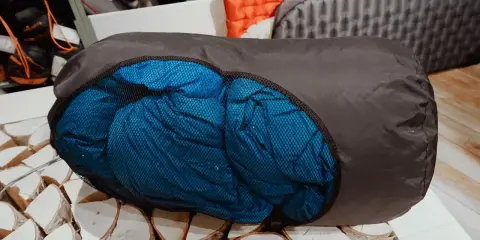 Ein blauer Schlafsack wird in einen dunklen Packsack gestopft, bereit für das nächste Abenteuer.