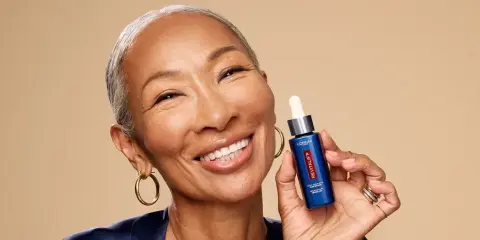 Mujer sonriente muestra un sérum Revitalift con retinol, ideal para rejuvenecer la piel y combatir arrugas.