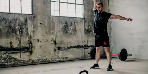 Mężczyzna wykonuje ćwiczenia z kettlebell, idealne dla początkujących. W tle sztanga i surowe wnętrze.