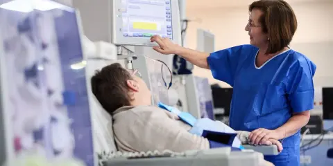 Pielęgniarka monitoruje parametry pacjenta po dializie. Pacjent leży, czując osłabienie po zabiegu.