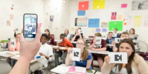 Classe che usa un'app per la scuola, con studenti che mostrano carte con simboli.