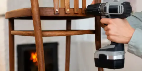 Persona repara una silla de madera con taladro. Un tornillo pasado de rosca dificulta la tarea.