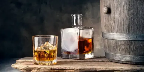 Szklanka z lodem i butelka whisky obok drewnianej beczki. Idealne połączenie, by dowiedzieć się, z czym pić whisky.