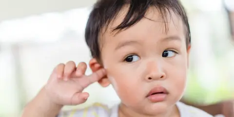Niño asiático se mete el dedo en la oreja, quizás para quitarse la suciedad detrás de las orejas.