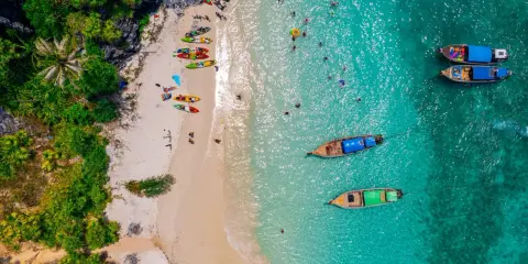 Rajska plaża na tajlandzkiej wyspie Phuket. Kajaki czekają na plaży, a turyści kąpią się w turkusowej wodzie.