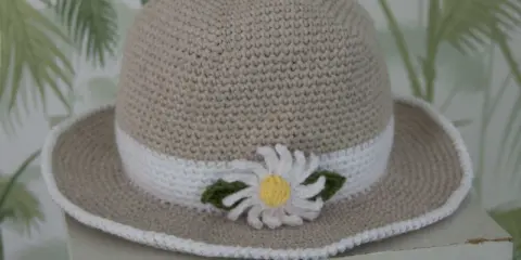 En virkad solhatt för barn, beige med vit kant och en söt blomdekor. Perfekt för soliga dagar!