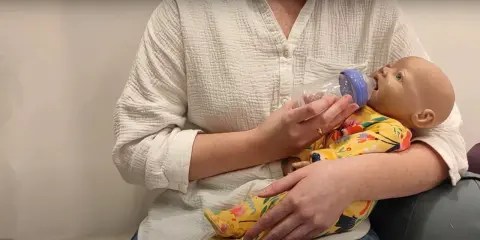 Nauka, jak karmić noworodka butelką, jest kluczowa. Na zdjęciu widzimy, jak prawidłowo karmić niemowlę butelką, trzymając je w ramionach.