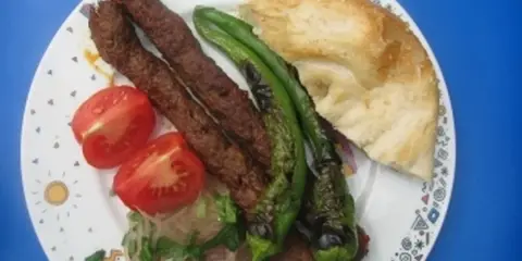 Adana Kebap mit gegrillten Peperoni, Tomaten und Fladenbrot auf einem Teller.