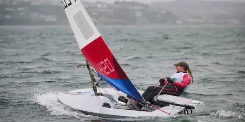 Jeune navigatrice en dériveur **tabur 320**, voile rouge et bleue, naviguant sur une mer agitée.