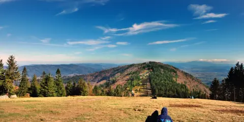 Widok na Beskid Śląski z Bielska-Białej. Dwie osoby siedzą na trawie, podziwiając panoramę gór.