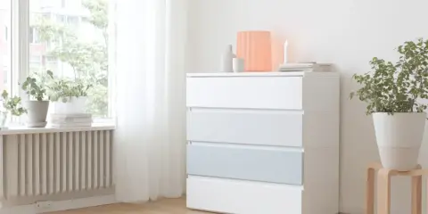 Eine weiße MALM Kommode mit vier Schubladen, eine davon hellblau, steht neben einem Fenster. Darauf sind Deko-Objekte und eine Kerze.