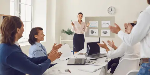 Uśmiechnięta kobieta kończy prezentację po angielsku. Zespół klaszcze, doceniając jej pracę.