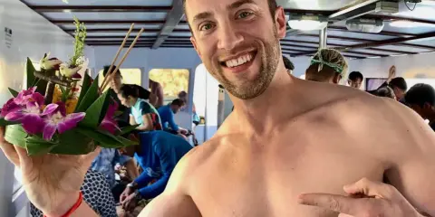 Smiling man on a boat in Asia, holding a flower offering. A perfect moment for gay travel in Asia.