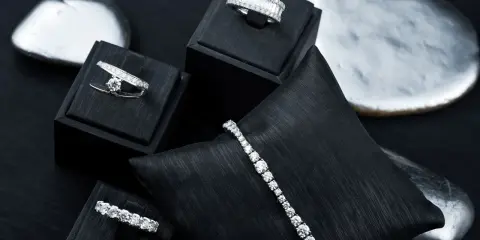 Gioielli scintillanti, anelli e bracciali con diamanti, esposti su supporti neri e pietre levigate.