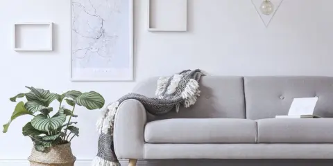 Przytulny salon z szarą kanapą, ozdobioną narzutą. Na ścianie mapa Sydney i geometryczna lampa.
