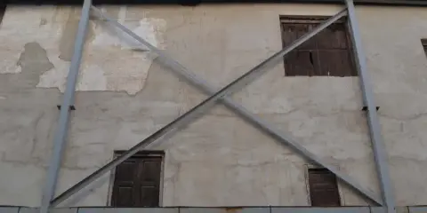 Estructura metálica en forma de X que refuerza una pared de concreto con ventanas de madera. La riostra, en este caso, es un elemento de soporte crucial.