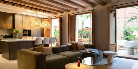 Salón moderno con vigas de madera vistas, sofá modular, cocina integrada y acceso a patio. Ideal para poner falso techo y unificar espacios.