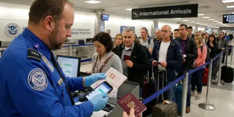 Funkcjonariusz służby celnej sprawdza paszporty w kolejce do odprawy na lotnisku.