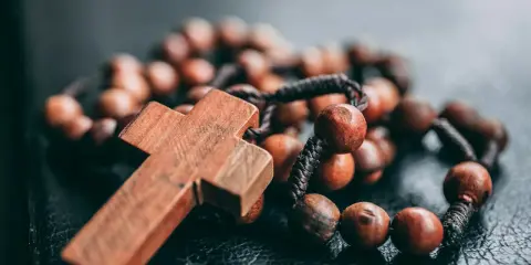 Drewniany krzyż i paciorki różańca, symbol wiary i modlitwy. Jeden dziesiątek różańca leży na ciemnym tle.