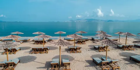 Pusta, słoneczna plaża na Kos, z rzędami leżaków i parasoli z trawy, czeka na gości.