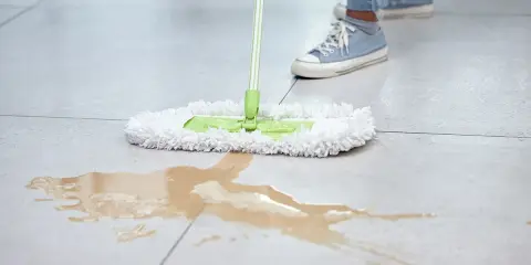 Mycie gres szkliwiony: mokra plama na jasnych płytkach i biały mop z zieloną rączką.