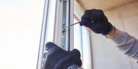 Ręce w rękawiczkach dokonują regulacji drzwi zewnętrznych PCV, dokręcając śrubę kluczem.