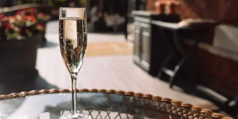Ein Glas Sekt auf einem Tisch im Freien. Auch wenn Sekt kein Verfallsdatum hat, sollte er frisch genossen werden.