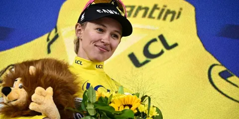 Kasia Niewiadoma strahlt im gelben Trikot, hält einen Löwen-Plüschtier und Blumen.
