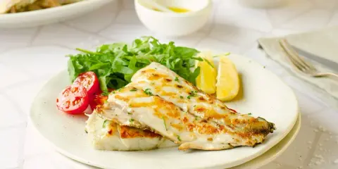 Deliciosa corvina a la plancha, servida con rúcula fresca, tomates cherry y gajos de limón. Un plato ligero y sabroso.