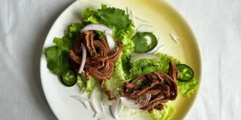 Crujiente oreja de cerdo frita servida sobre lechuga con cebolla morada, cilantro y jalapeño.