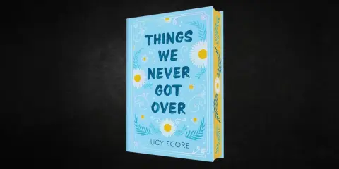 Okładka książki "Things We Never Got Over" Lucy Score. Jasnoniebieska okładka z motywem stokrotek i liści.