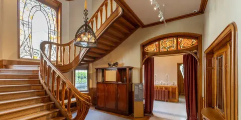 Escalier majestueux en bois, vitraux colorés, mobilier ancien. Un intérieur d'une élégance intemporelle, évoquant le style Majorelle.