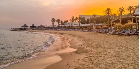 Strand in Tunesien im Oktober: Sanfte Wellen, Palmen und Liegestühle unter einem warmen Sonnenuntergang. Perfektes Wetter für einen entspannten Urlaub.