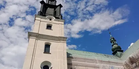 Wieża kościoła w Gidlach pod błękitnym niebem z chmurami. Widać fragment dachu w rusztowaniach.