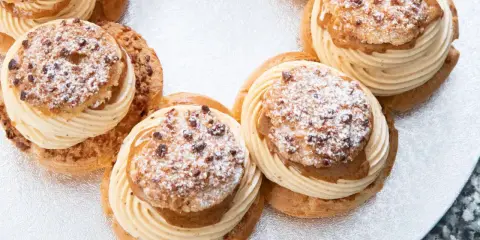 Plusieurs Paris-Brest, des pâtisseries rondes à la pâte à choux garnies de crème onctueuse et saupoudrées de sucre glace et d'amandes.