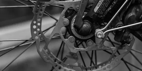 Zbliżenie na tarczę hamulcową i piastę roweru. Widać mechanizm przerzutki Shimano i ostrzeżenie na ramie.