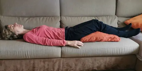 Donna sdraiata sul divano con un cuscino sotto le ginocchia per una postura corretta seduti divano.